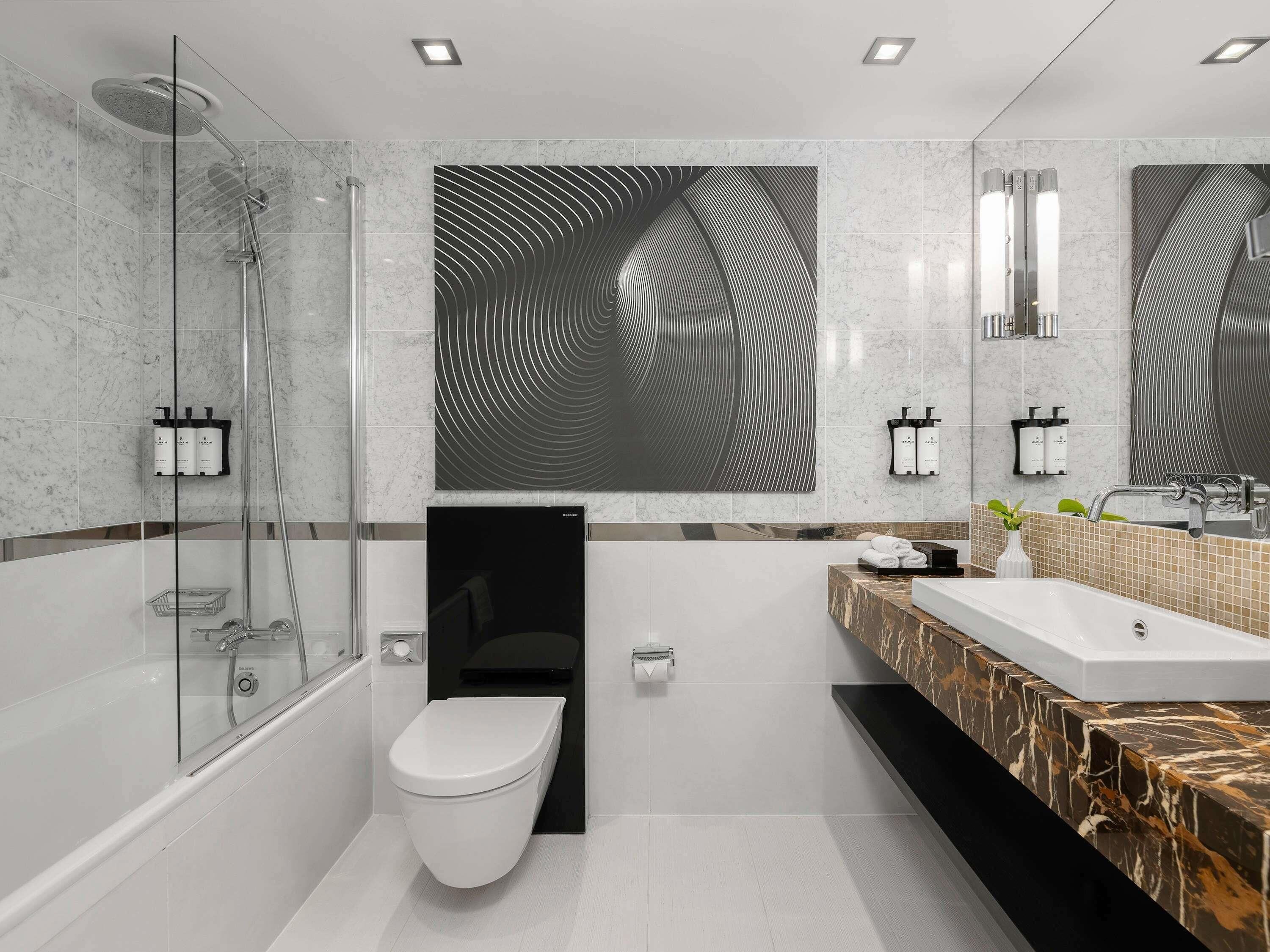 A modern bathroom with a glass shower enclosure, a toilet, a sink with a marble countertop, and a large mirror.