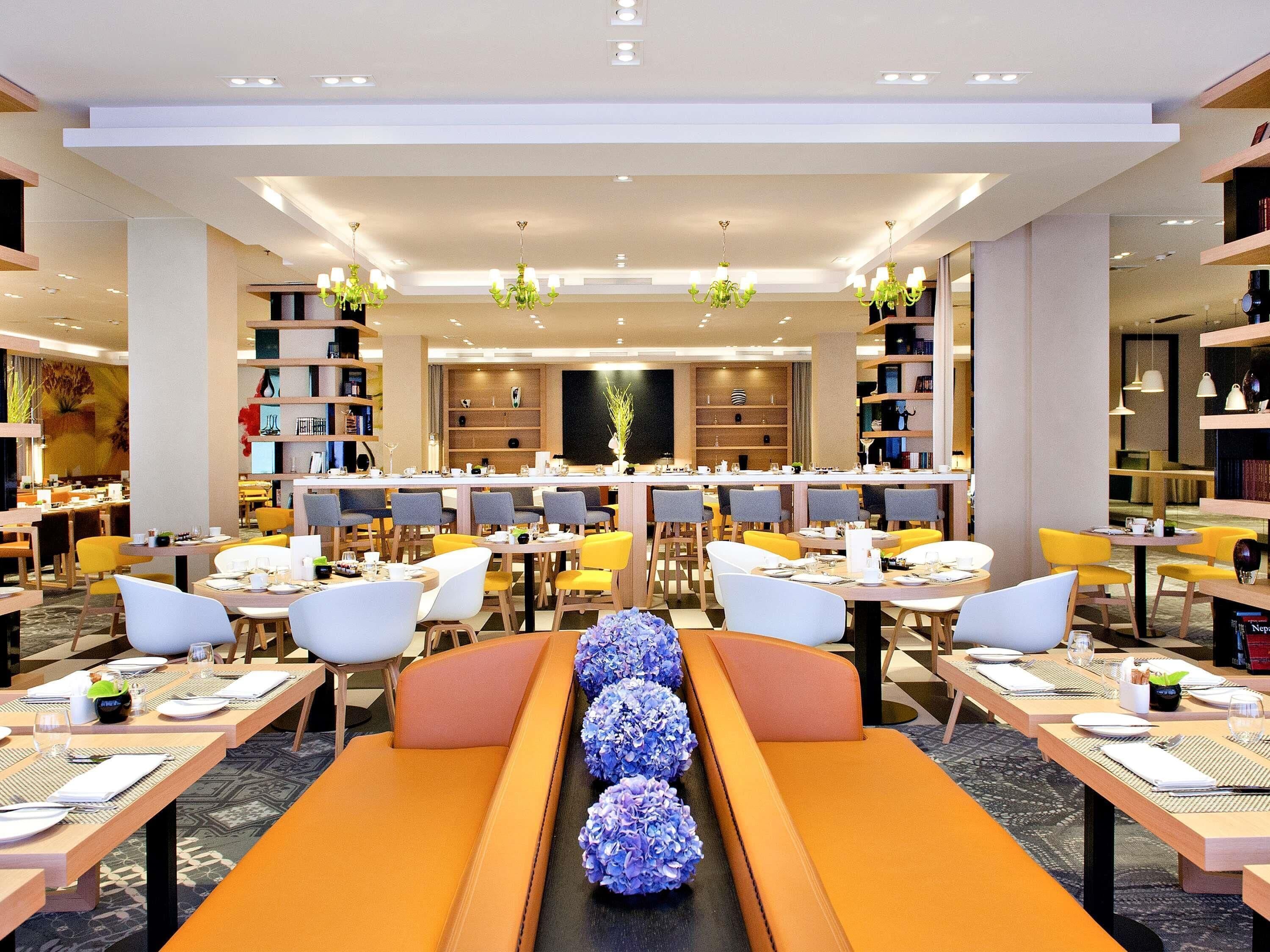 Un espace repas moderne, doté de plusieurs tables et chaises, d’une composition décorative centrale et d’étagères disposées sur les côtés.