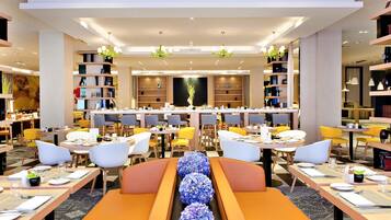 Un espace repas moderne, doté de plusieurs tables et chaises, d’une composition décorative centrale et d’étagères disposées sur les côtés.