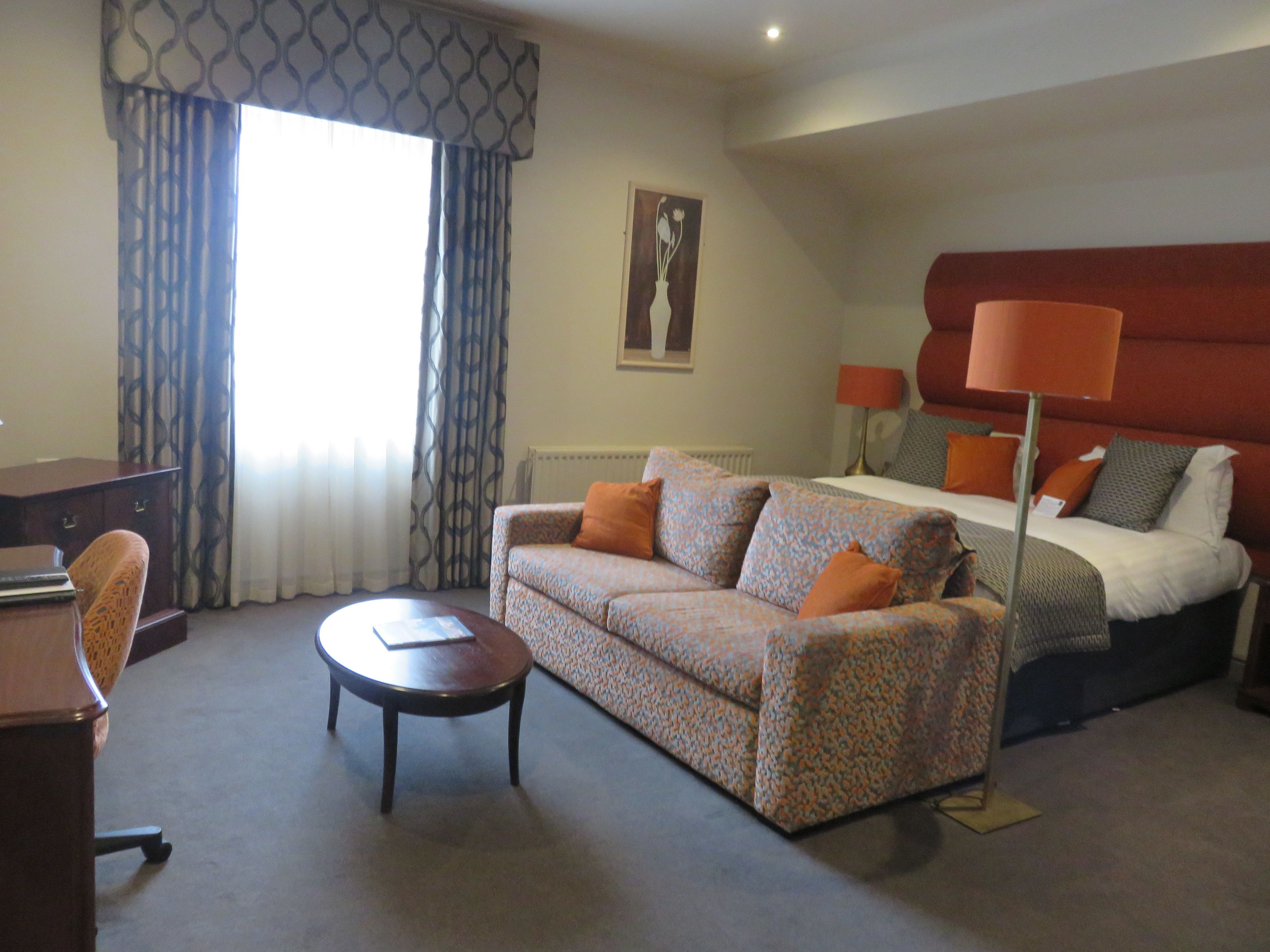 A hotel room with a sofa, a desk, a bed, and a lamp.