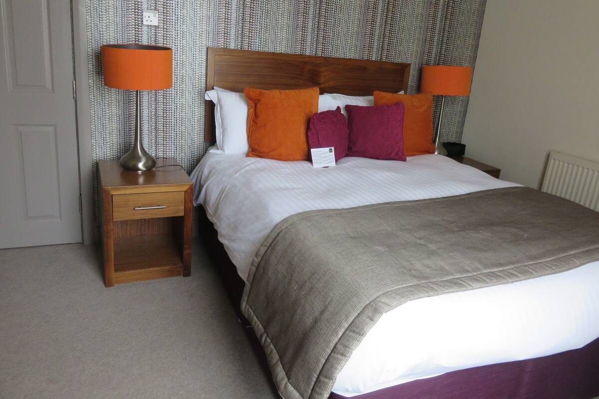 A neatly made bed with a wooden headboard, two bedside tables with lamps, and a patterned wallpaper.