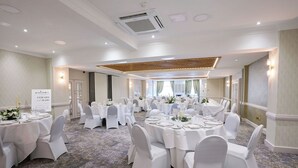 A banquet hall with round tables set for dining, white chairs, and a carpeted floor. - The Belmont Hotel (Leicester)