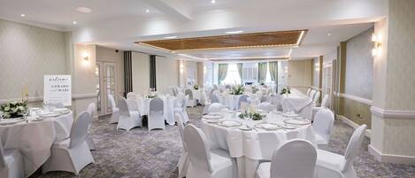 A banquet hall with round tables set for dining, white chairs, and a carpeted floor.