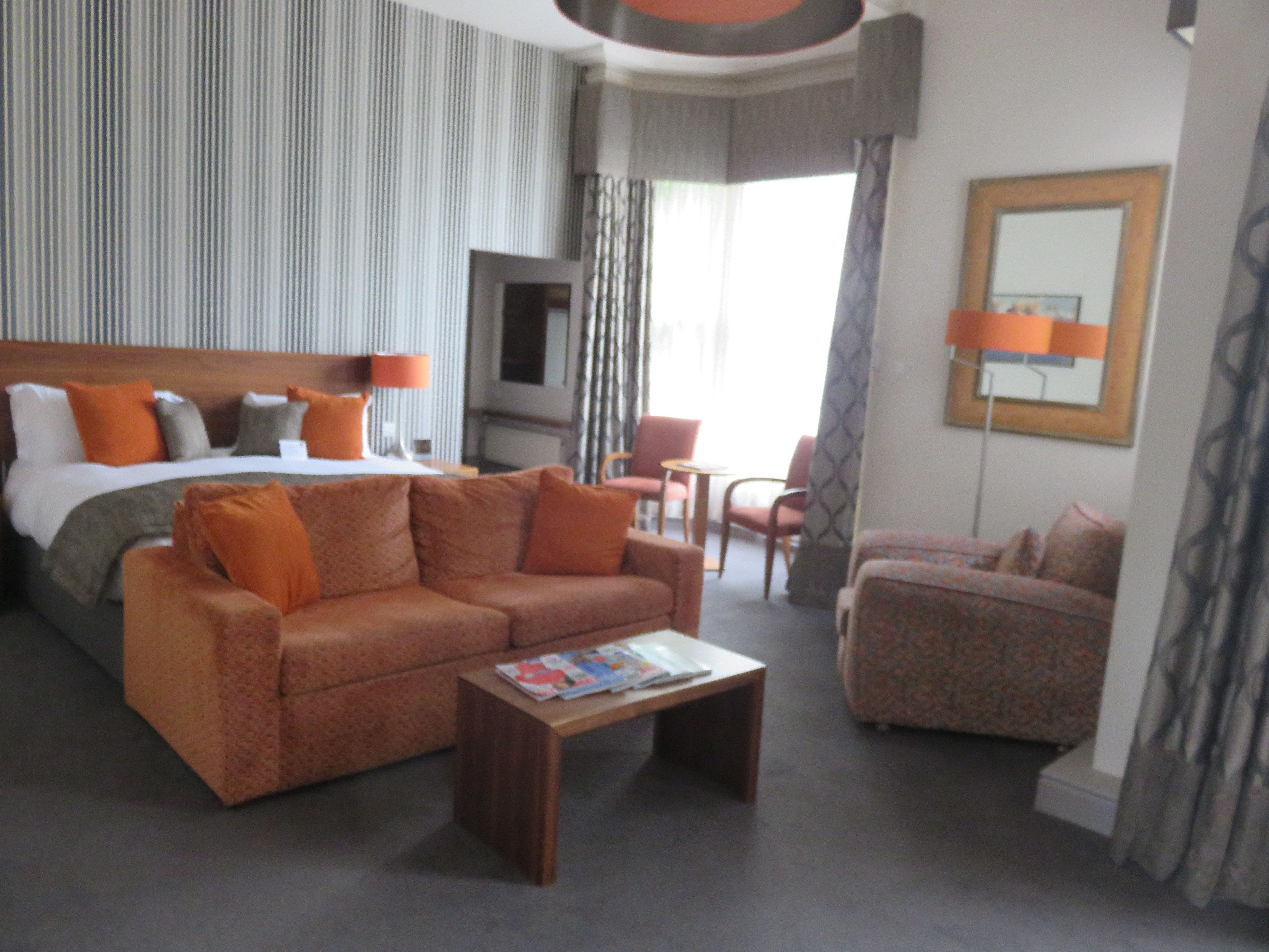 A hotel room with a bed, two sofas, a coffee table, a TV, and a mirror.
