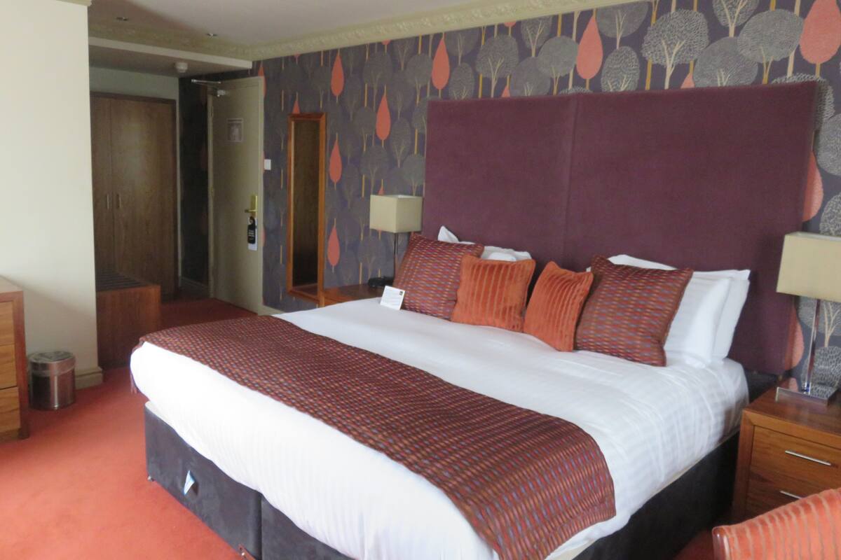 A hotel room with a large bed, two bedside tables, a wardrobe, and a door leading to another room.
