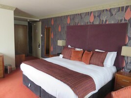 A hotel room with a large bed, two bedside tables, a wardrobe, and a door leading to another room.