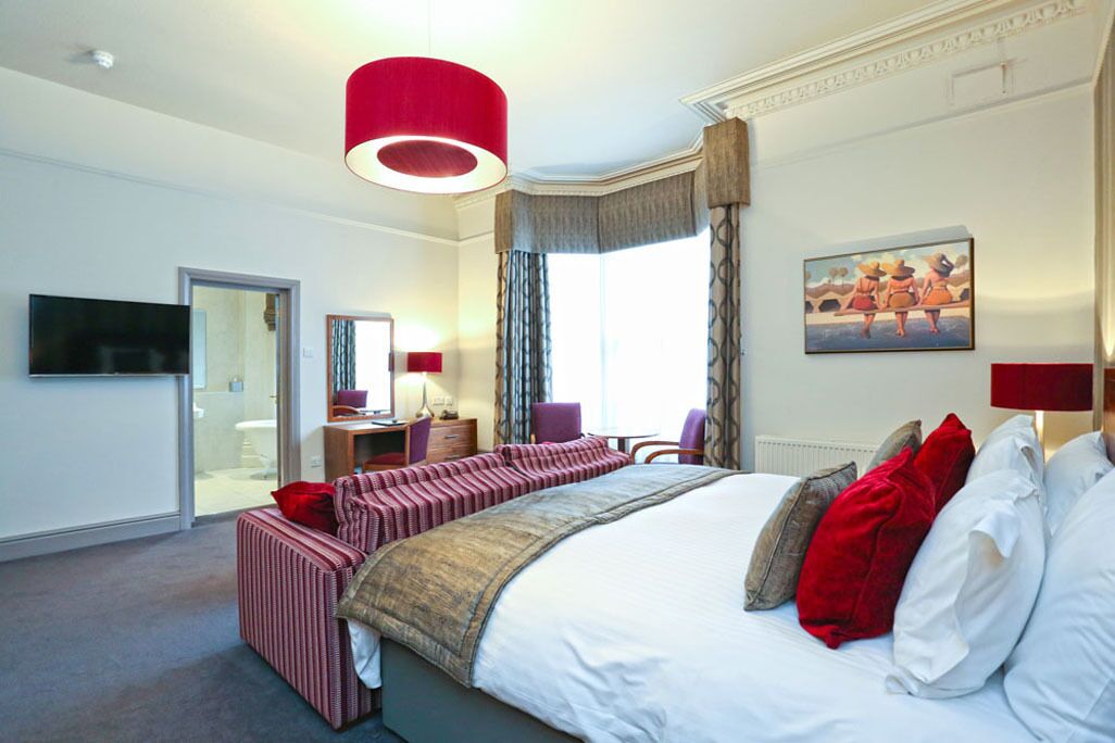 A hotel room with a large bed, a desk, a chair, a TV, and a window with curtains.
