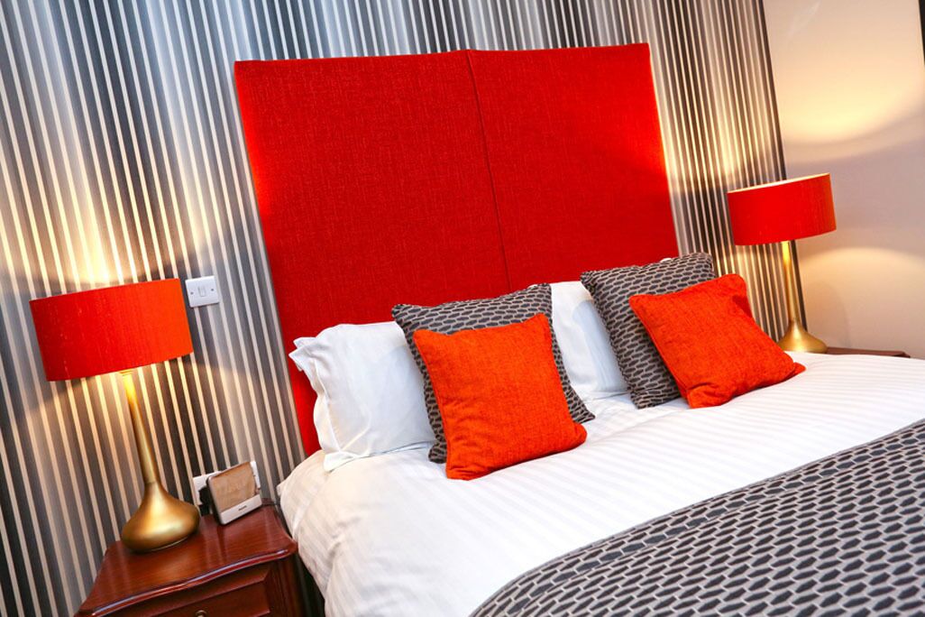 A hotel room with a large bed, red and white bedding, and two bedside lamps.