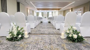 A wedding aisle with white chairs, a floral arrangement, and candles. - The Belmont Hotel (Leicester)