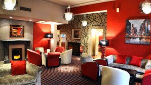 A modern lounge area with red and grey upholstered seating, a patterned carpet, and a fireplace. - The Belmont Hotel (Leicester)