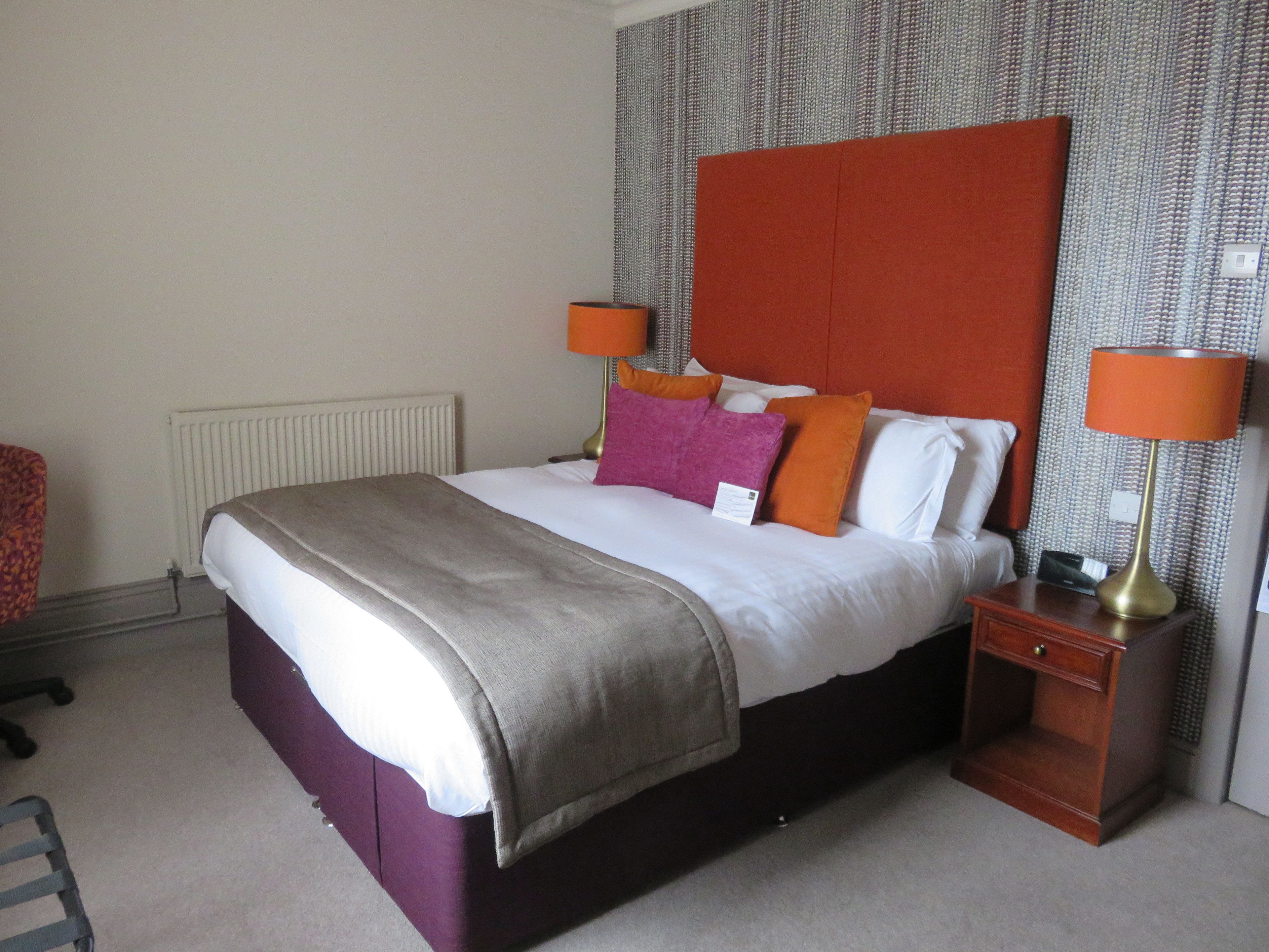 A hotel room with a large bed, two bedside tables, a chair, and a radiator.