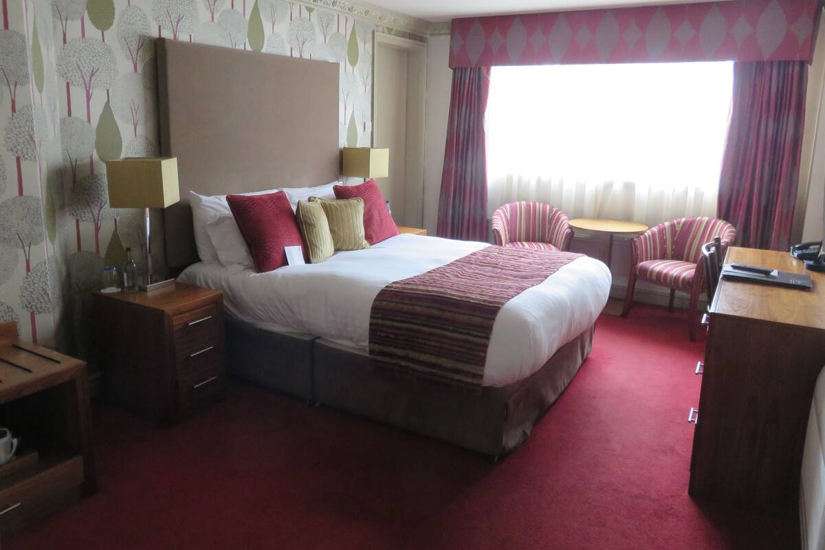A hotel room with a large bed, a desk, a chair, and a small table.