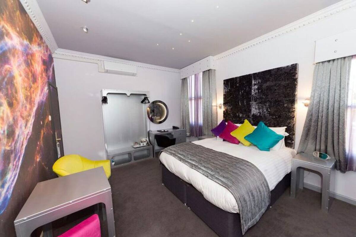 A modern bedroom with a large bed, a desk, a chair, and a mirror.