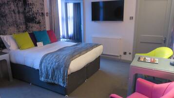 A hotel room with a bed, a TV mounted on the wall, a desk with a chair, and a door.