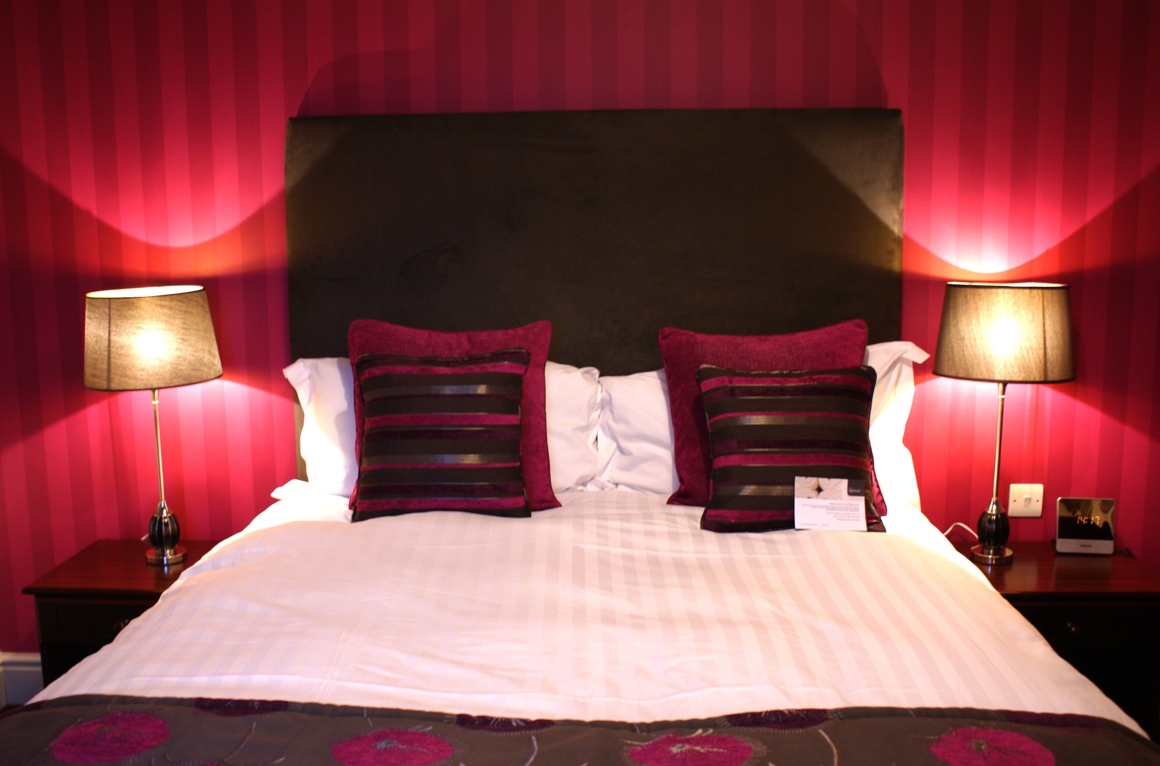 A neatly made bed with a dark headboard, two bedside lamps, and a red-striped wall.