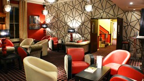A hotel lobby with red and beige seating, patterned walls, and a staircase leading to another area. - The Belmont Hotel (Leicester)