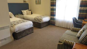 A hotel room with two beds, a sofa, a small table, and a window with curtains.