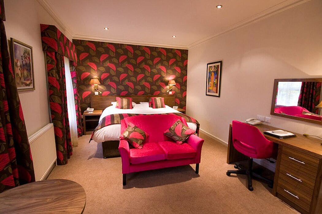 A hotel room with a bed, a desk, a chair, a red sofa, and a large mirror.