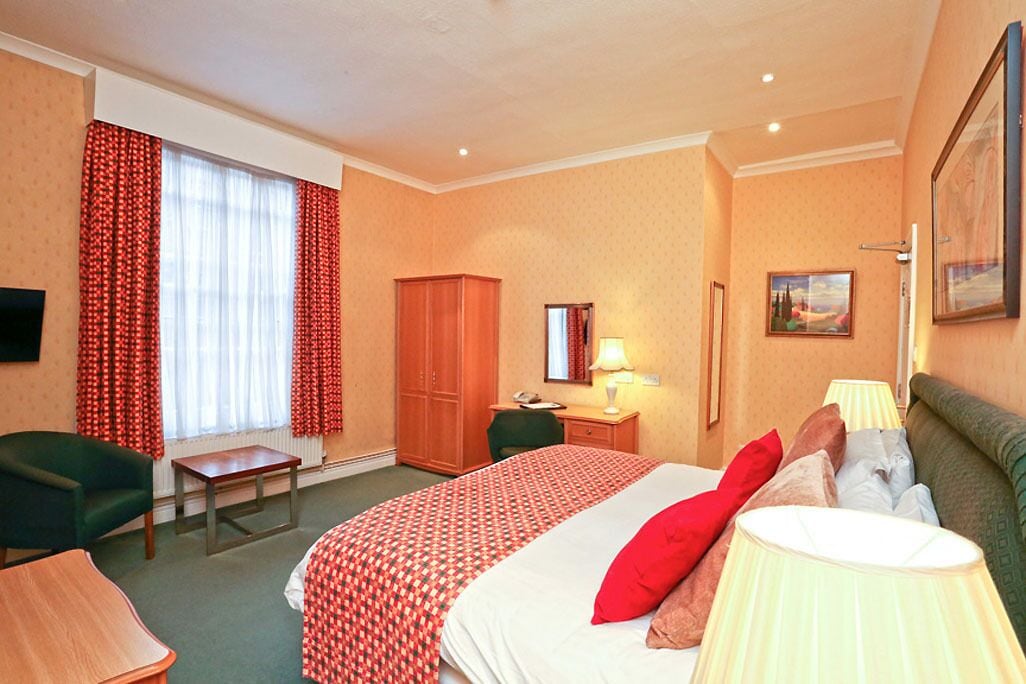 A hotel room with a bed, a desk, a chair, a wardrobe, and a television.