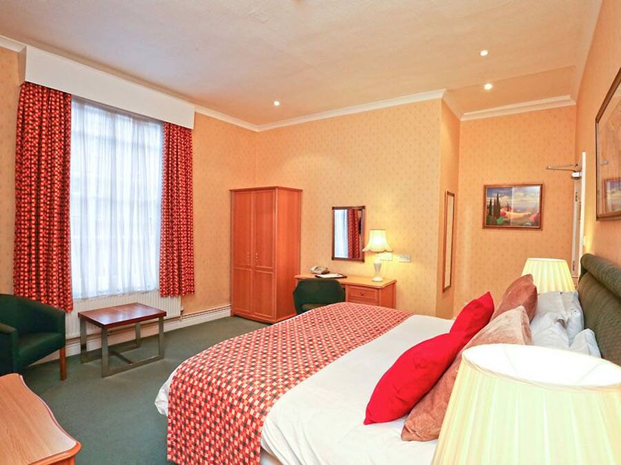 A hotel room with a bed, a desk, a chair, a wardrobe, and a television.