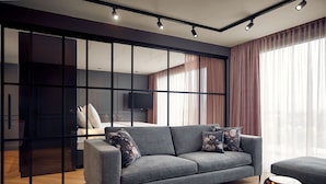 A modern living room with a grey sofa, a coffee table, and a TV. There is a sliding door leading to a bedroom. - Van der Valk Hotel Antwerpen (Antwerp)