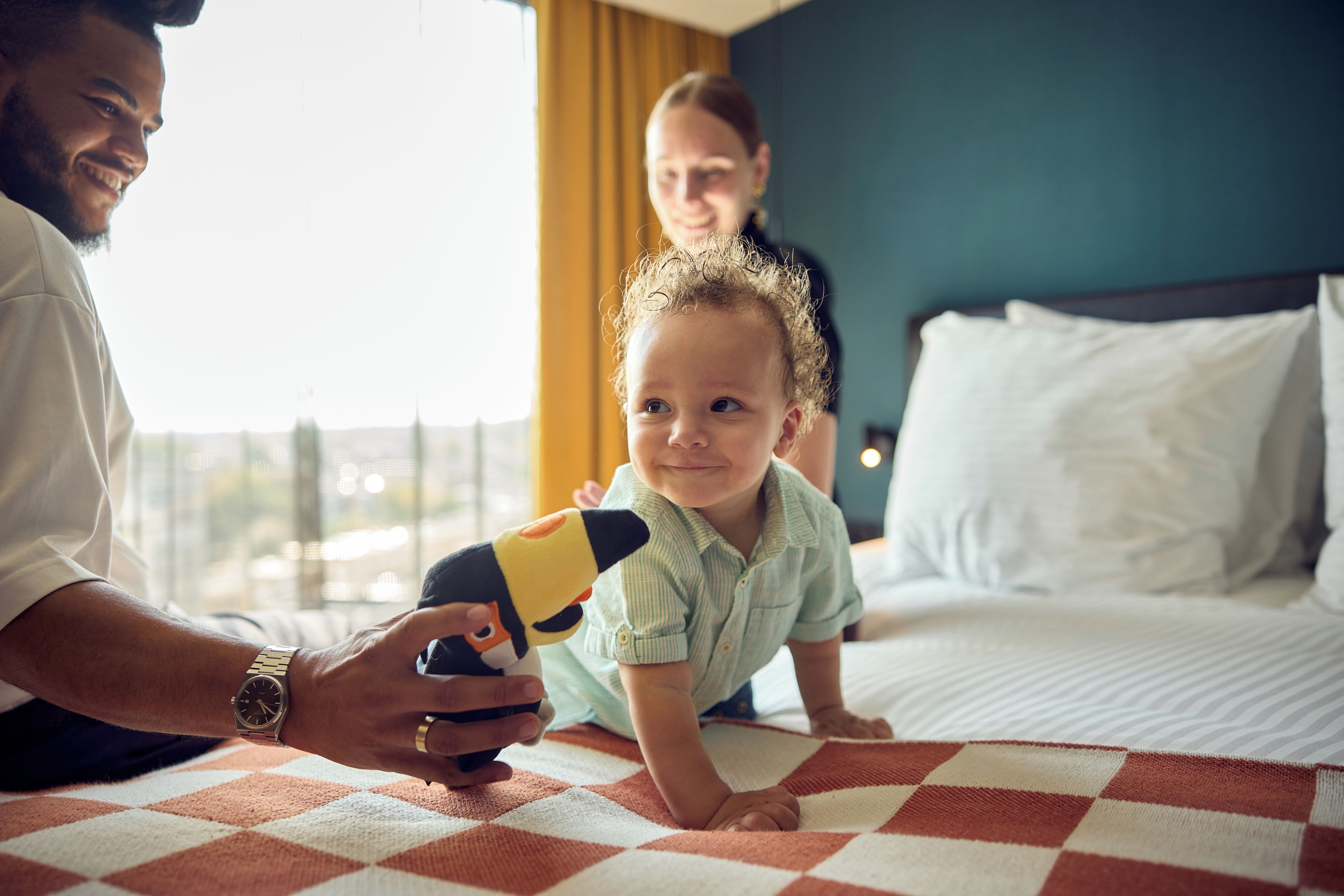 Een hotelkamer met een bed, een geruit plaid en een raam met gordijnen.