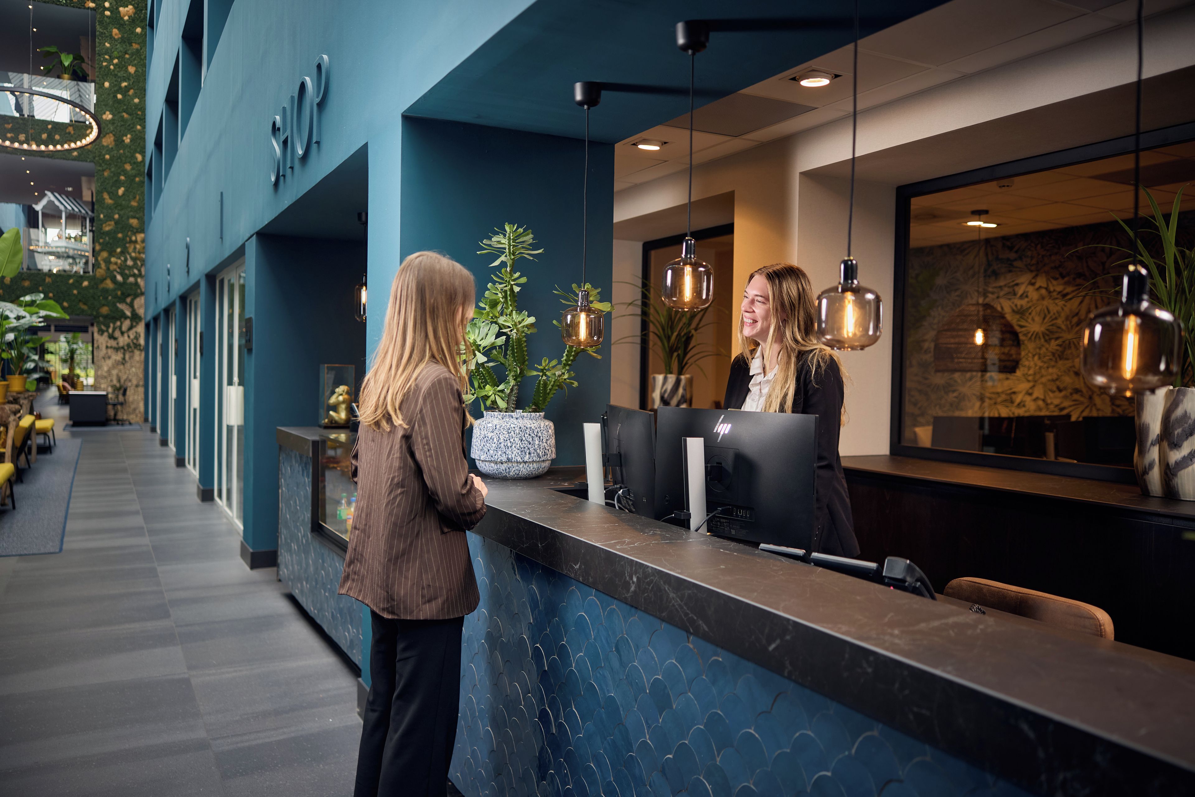 A reception desk with a modern design, a potted plant, and a large window with a view.