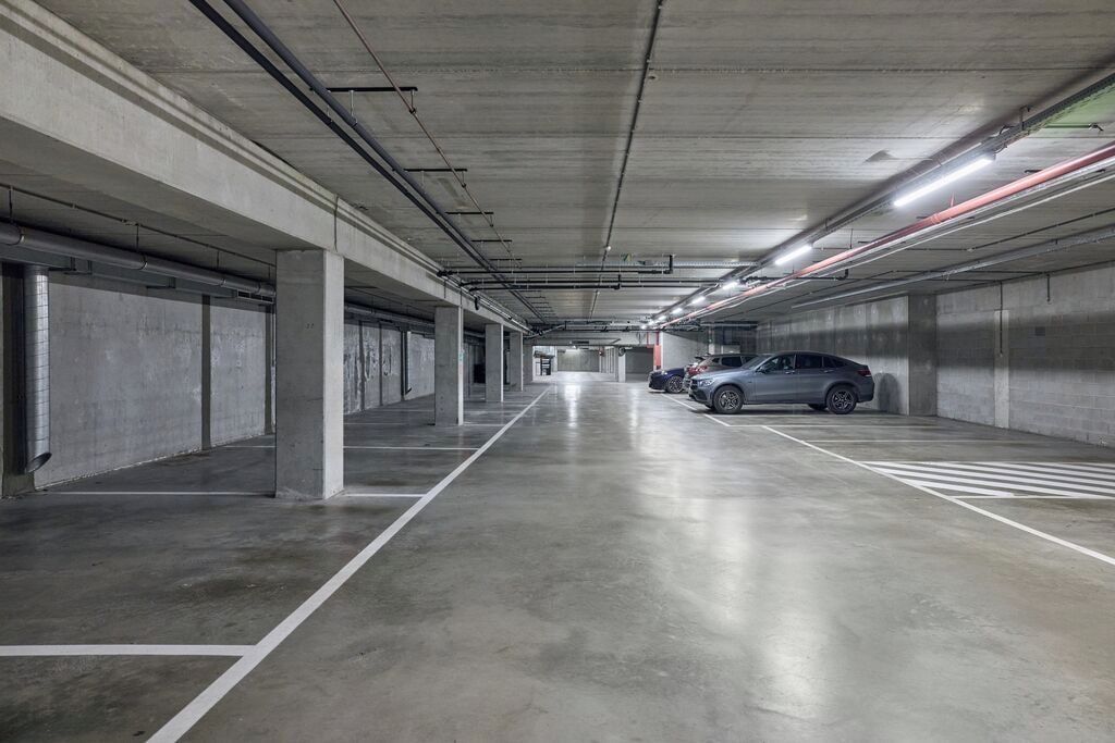 A multi-level parking garage with concrete pillars, fluorescent lighting, and marked parking spaces.