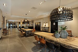 A modern dining area with a long wooden table, multiple chairs, and a unique geometric pendant light. - Van der Valk Hotel Antwerpen (Antwerp)