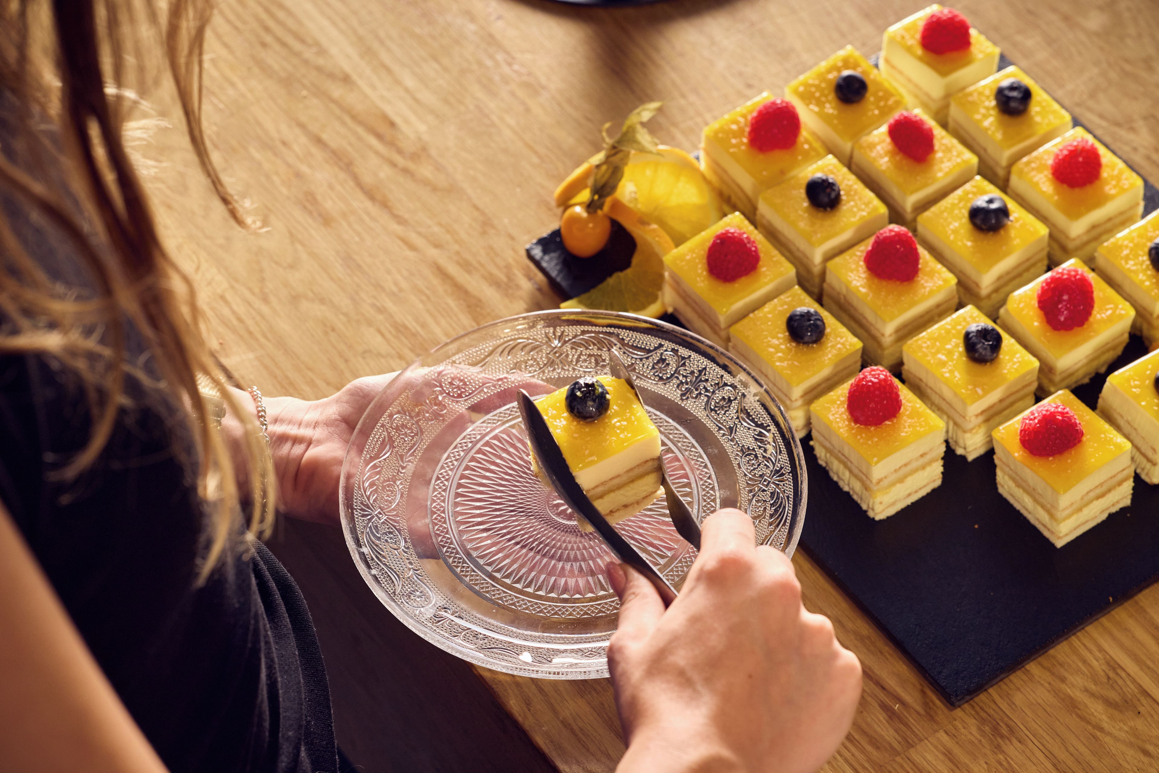 Une personne qui coupe un dessert avec un couteau sur une assiette en verre.