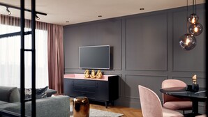 Una sala moderna con un sofá gris, un aparador rosa y negro, un televisor de pantalla plana y un comedor con sillas rosas.