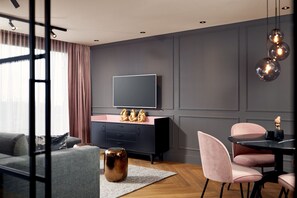 Una sala moderna con un sofá gris, un aparador rosa y negro, un televisor de pantalla plana y un comedor con sillas rosas.
