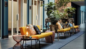 A modern indoor seating area with yellow sofas, patterned cushions, and a large potted plant. - Van der Valk Hotel Antwerpen (Antwerp)
