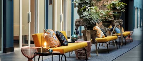 Un área de estar moderna en el interior, con sofás amarillos, cojines estampados y una planta grande en maceta.