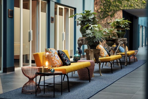 Un área de estar moderna en el interior, con sofás amarillos, cojines estampados y una planta grande en maceta.