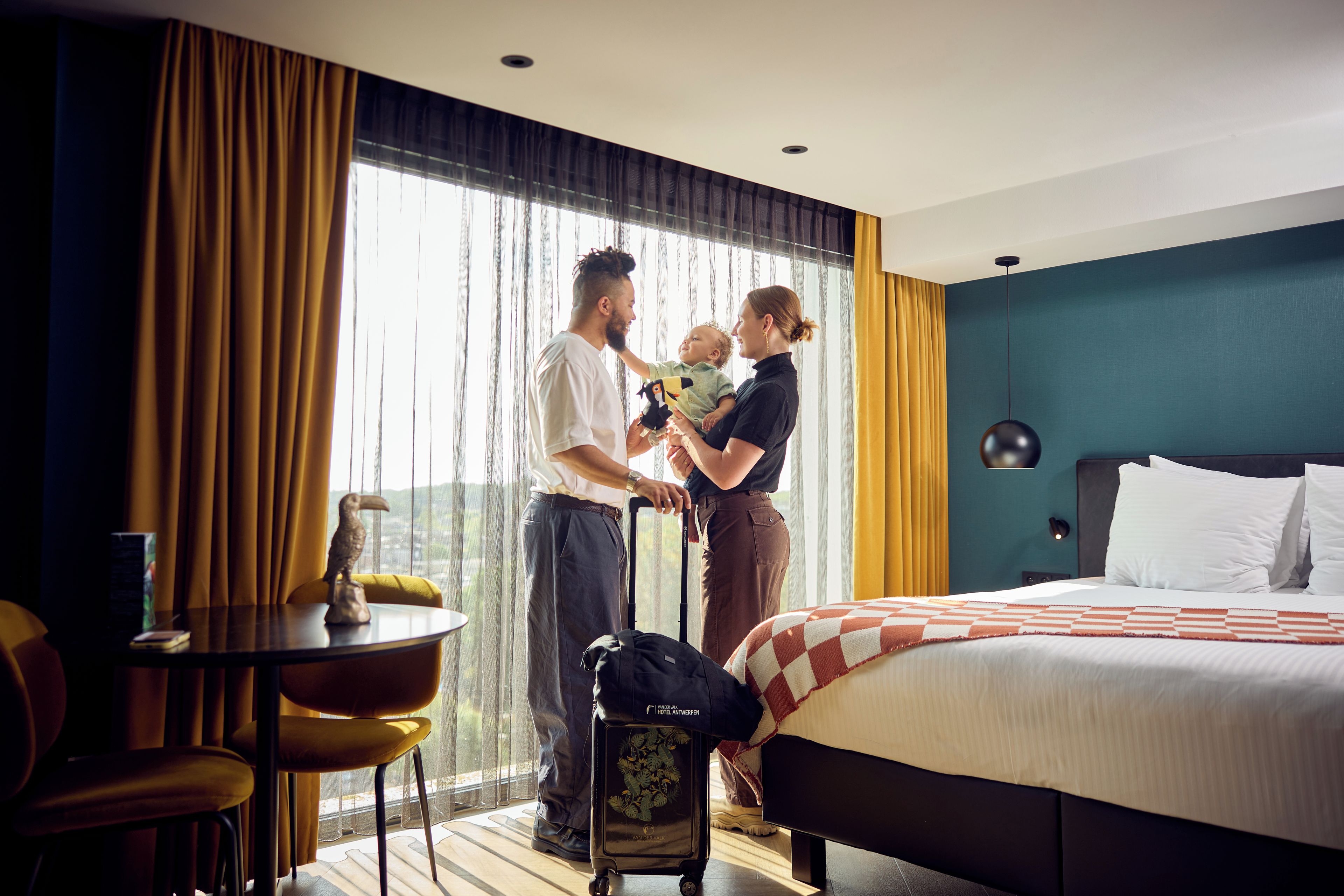 A hotel room with a bed, a chair, a table, and a window with curtains.