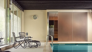 A pool area with a glass enclosure, a clock on the wall, and a seating area with chairs and a table. - Van der Valk Hotel Antwerpen (Antwerp)