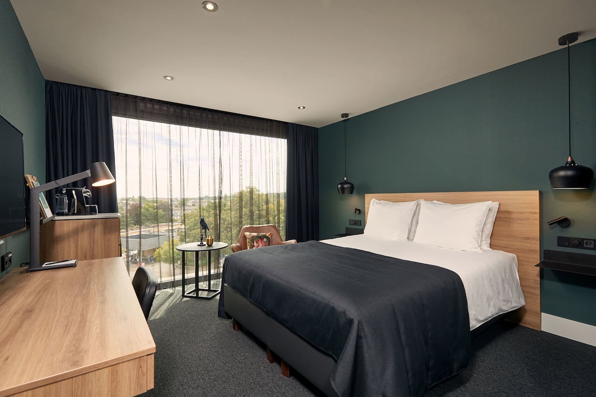 A modern hotel room with a large bed, a desk, a chair, and a small table.