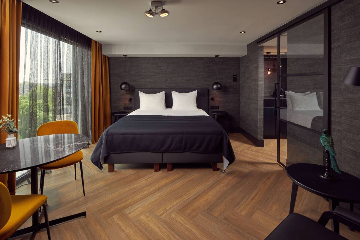 A modern hotel room with a large bed, a dining table, and a separate seating area.