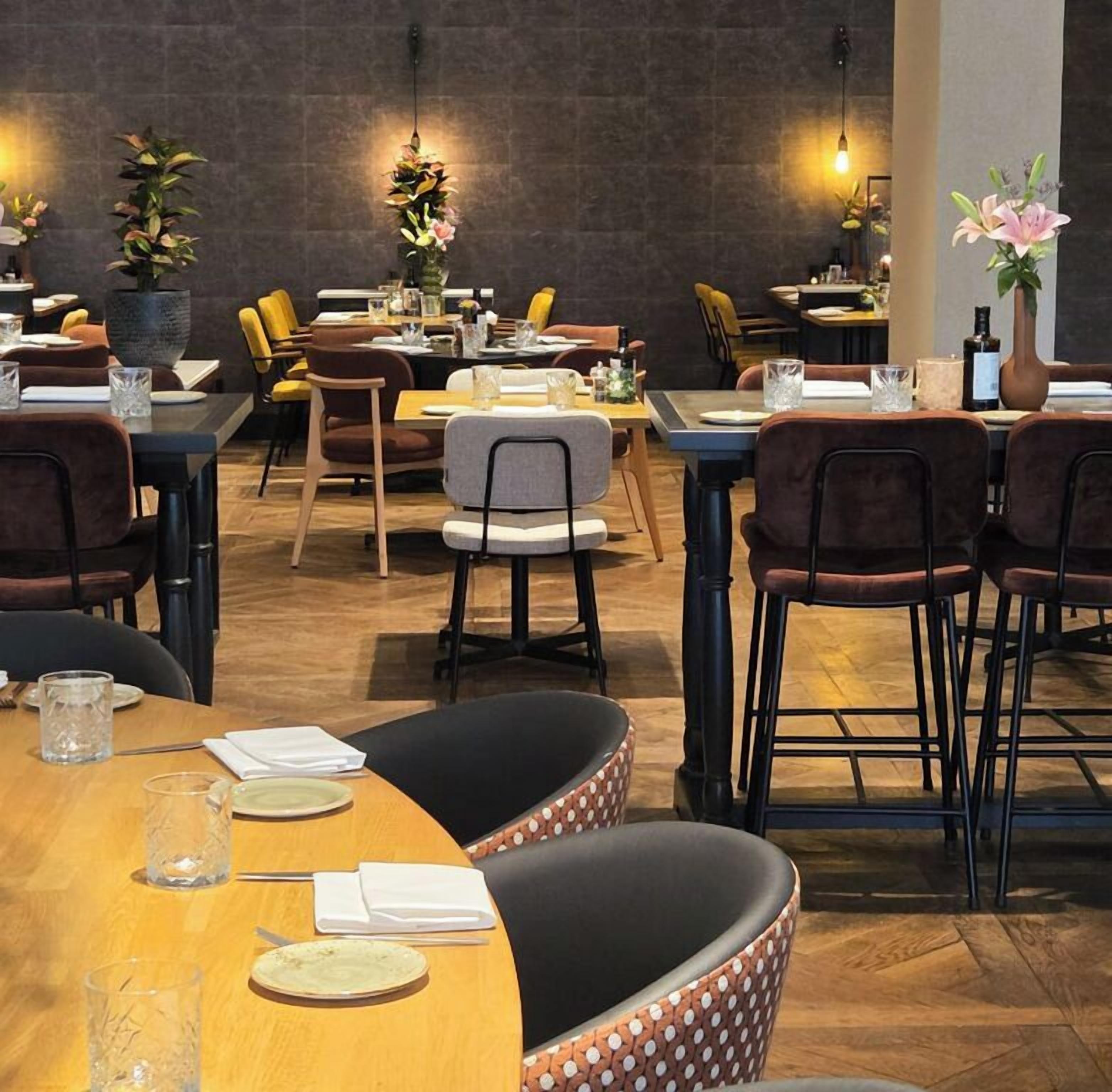 Un restaurant avec de nombreuses tables et chaises, dont certaines sont dotées de coussins. On y trouve des plantes en pot et un vase rempli de fleurs sur les tables.