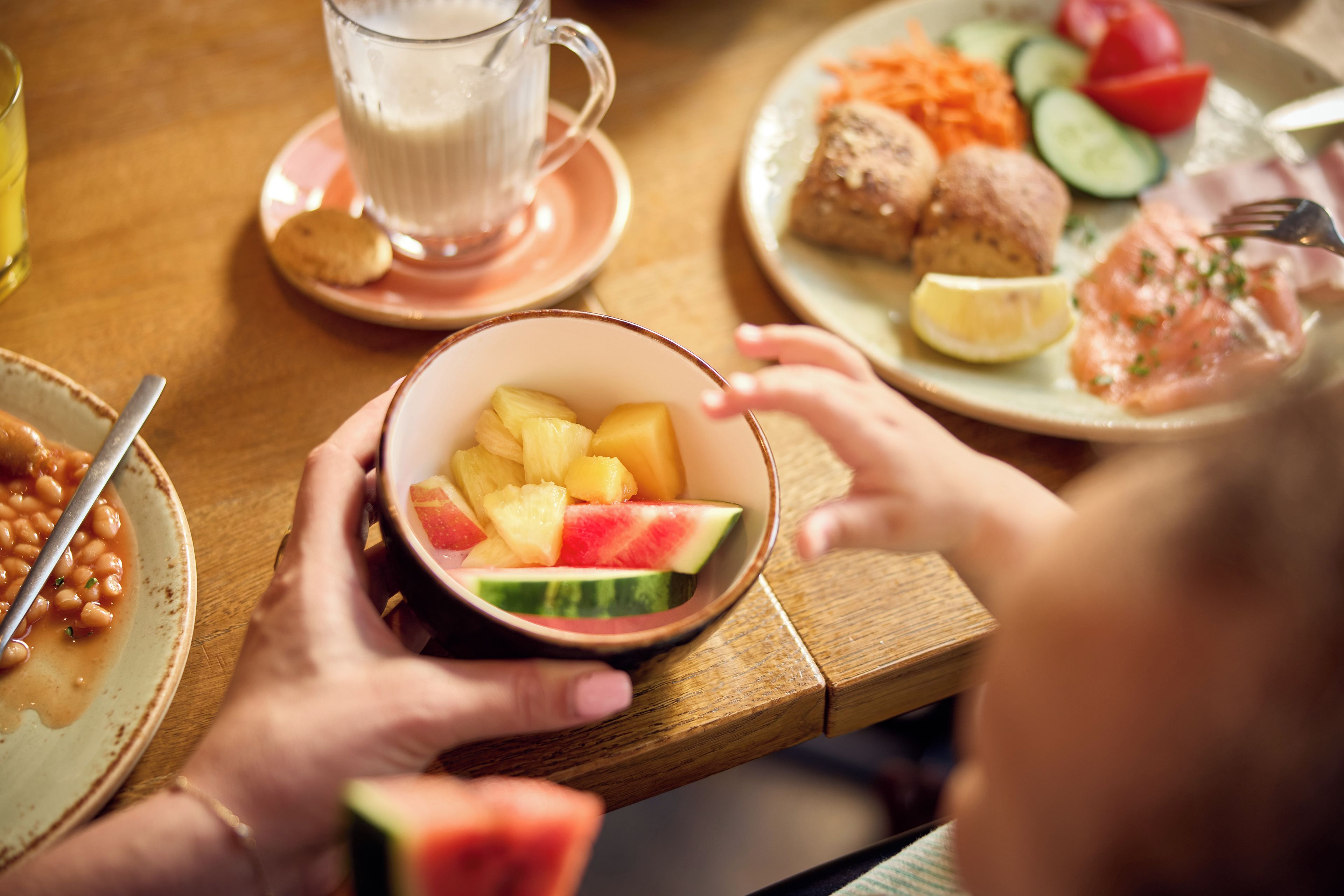 A dining table with a bowl of fruit, a plate with vegetables, and a cup of a beverage.