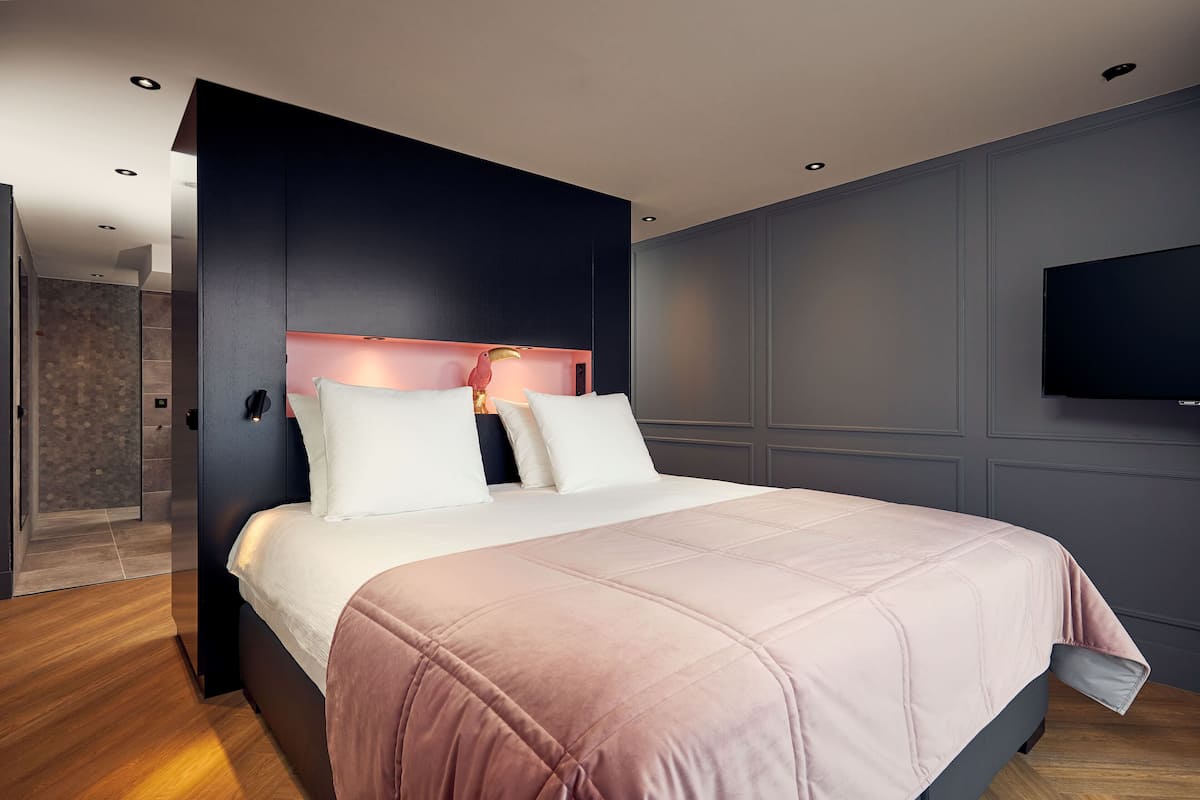 A modern bedroom with a large bed, a dark headboard, and a flat-screen TV on the wall.