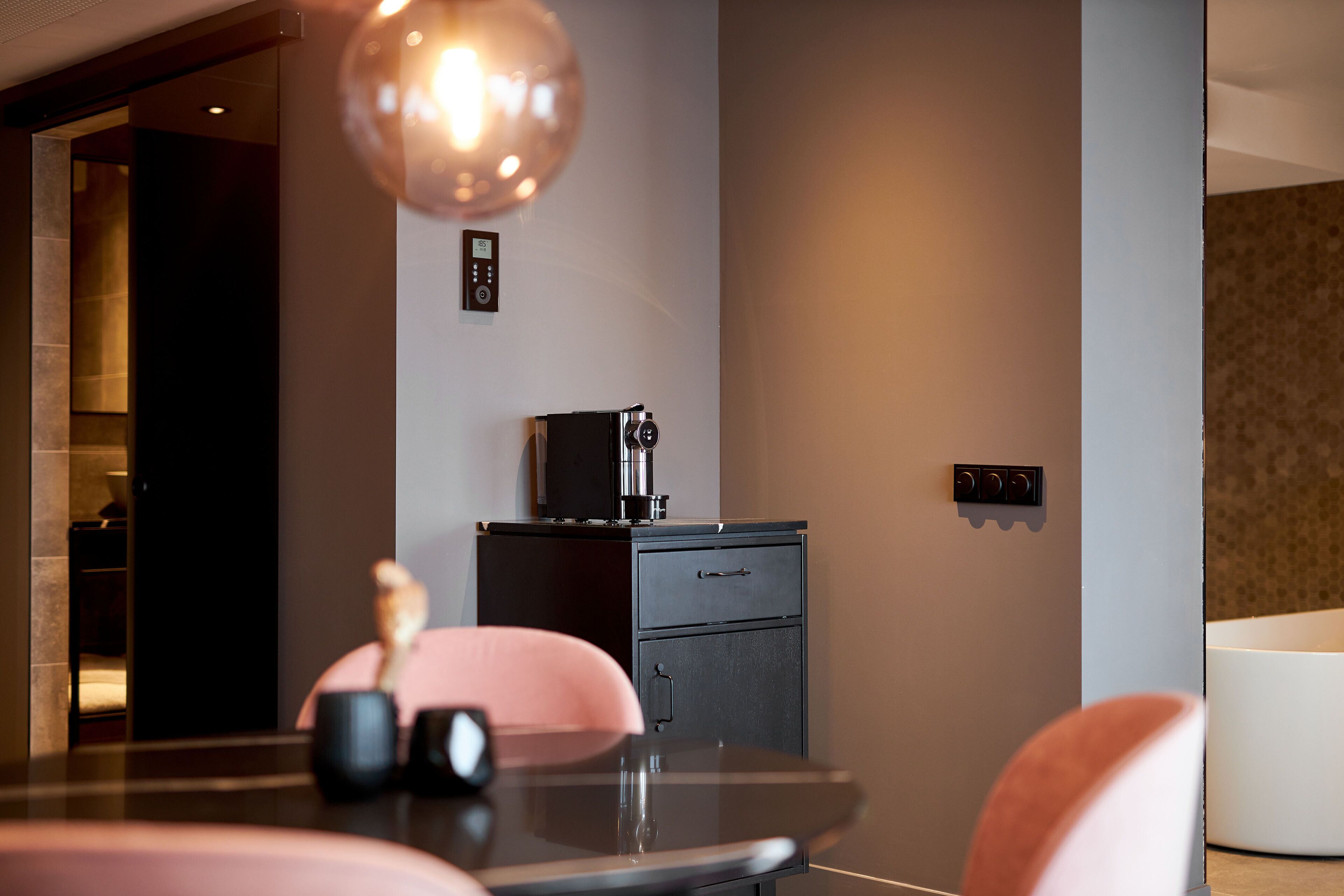A modern kitchen with a coffee machine, a small cabinet, and a dining area with a table and chairs.
