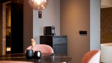 A modern kitchen with a coffee machine, a small cabinet, and a dining area with a table and chairs.