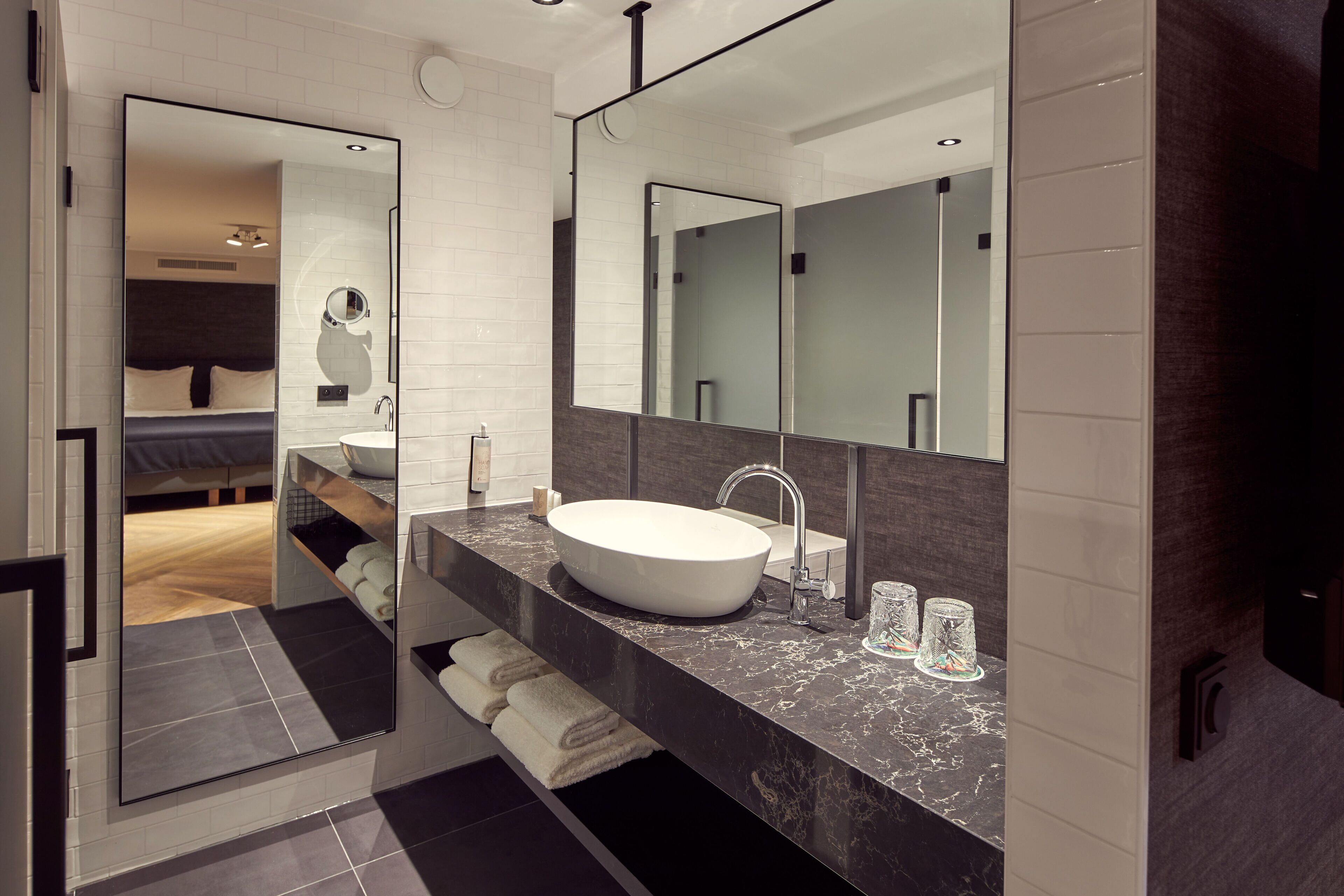 Une salle de bain moderne avec un grand miroir, un lavabo blanc et un plan de toilette en marbre foncé.