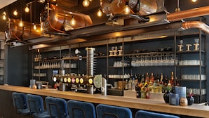 A bar area with blue bar stools, copper beer taps, and shelves stocked with bottles and glasses. - Van der Valk Hotel Antwerpen (Antwerp)