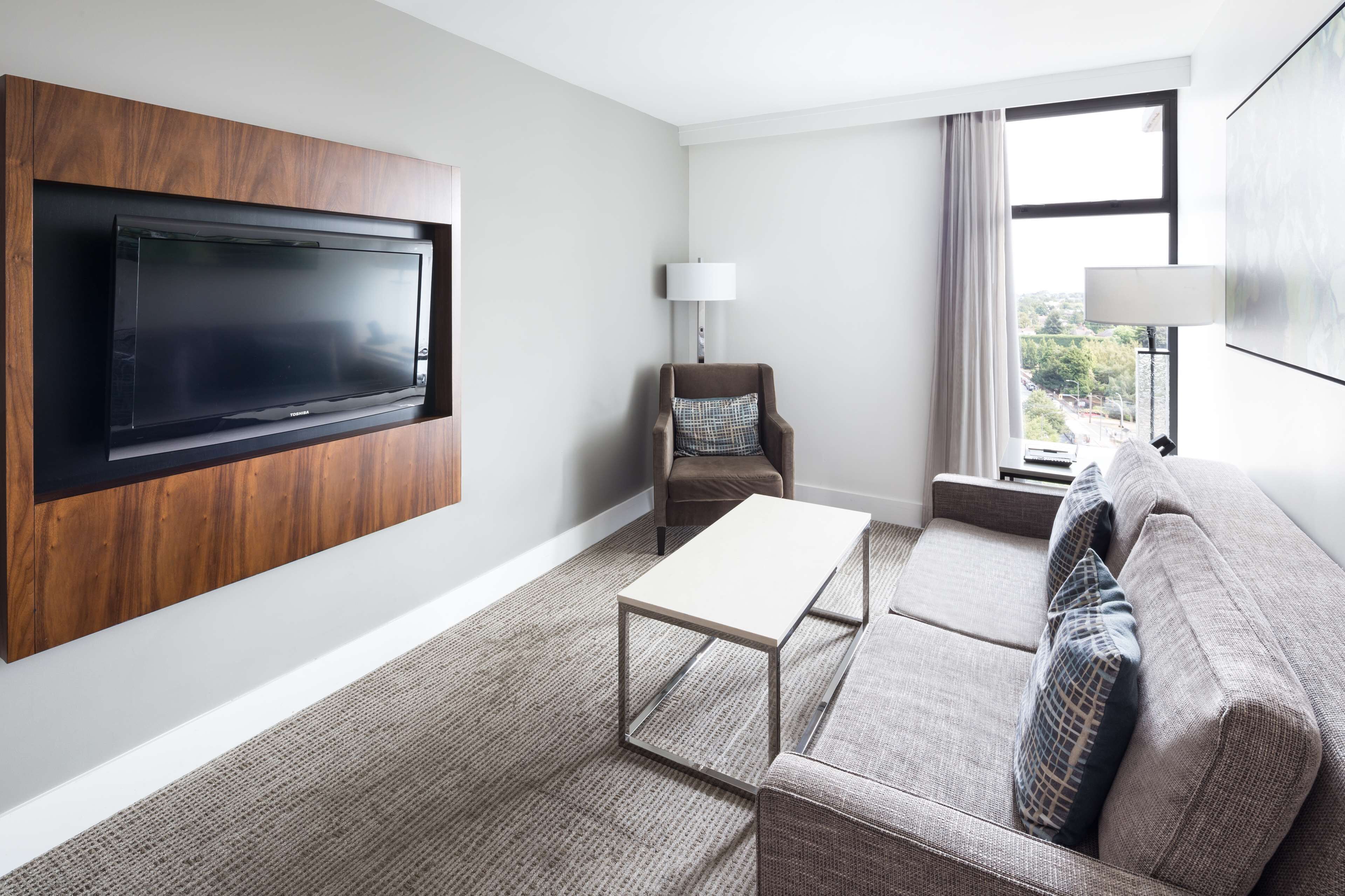 Une chambre d’hôtel moderne équipée d’un téléviseur à écran plat fixé au mur, d’un canapé, d’une petite table et d’une chaise.