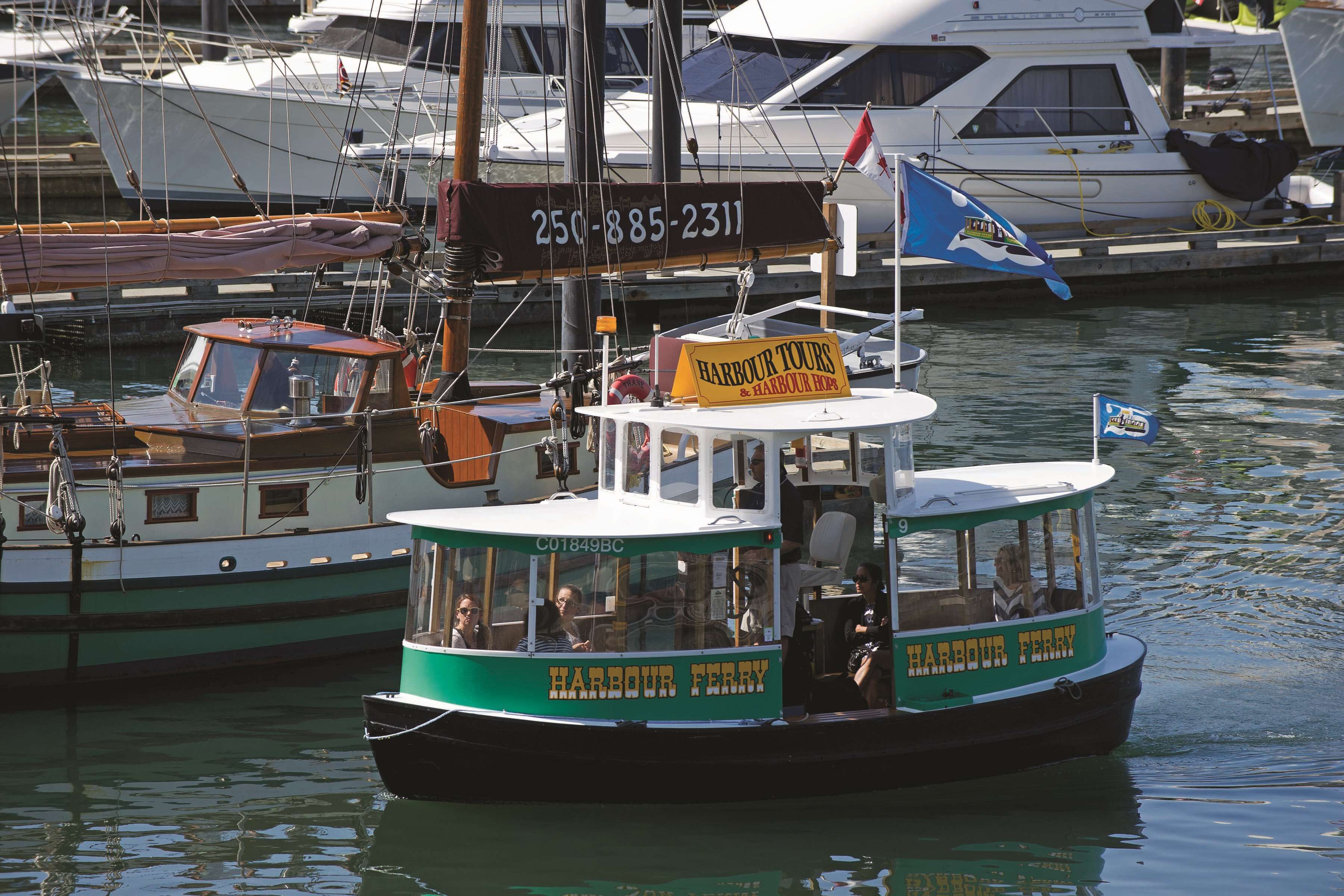 Un ferry del puerto con un cartel, pasajeros y otras embarcaciones al fondo.