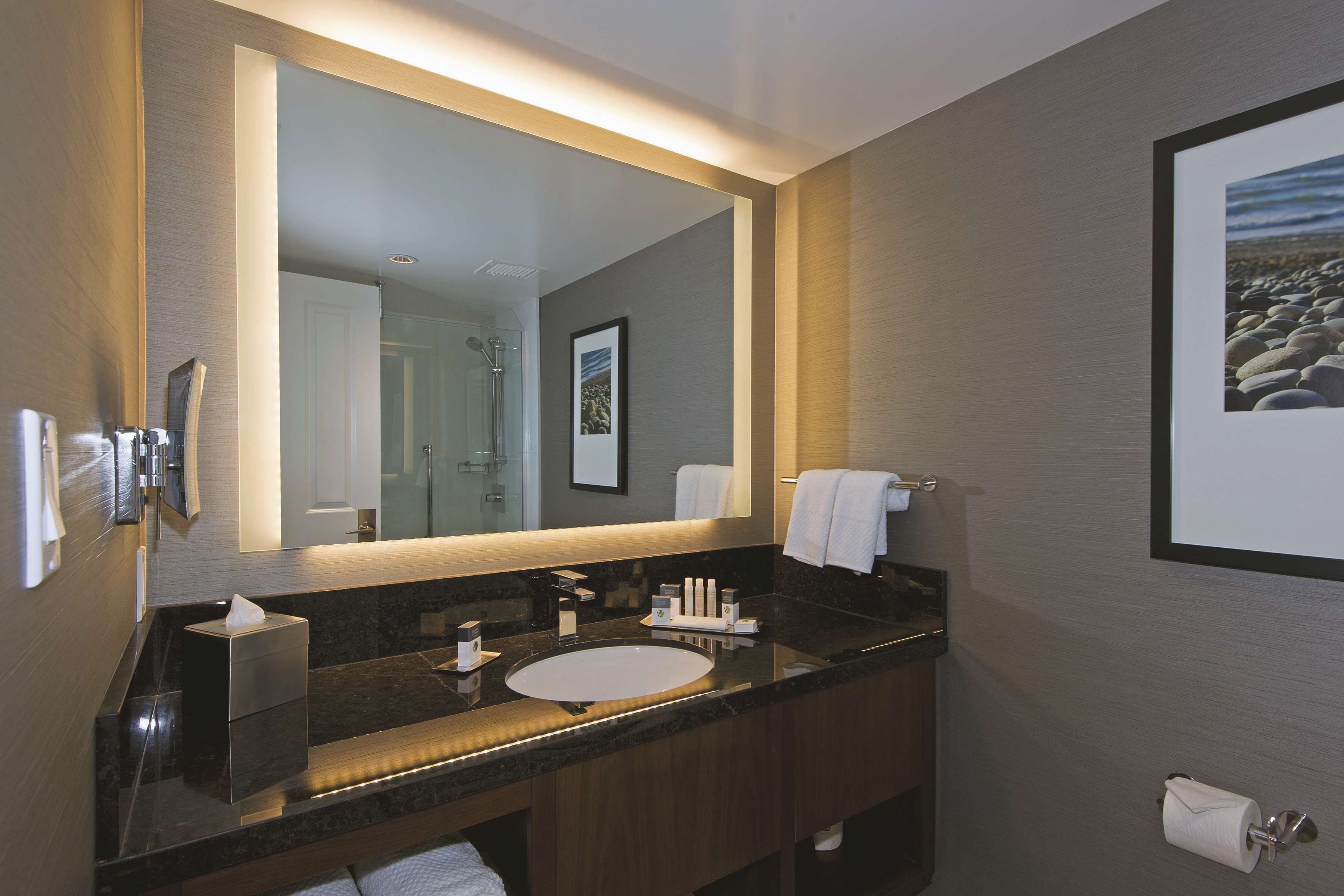A modern bathroom with a large mirror, a sink, and a toilet.