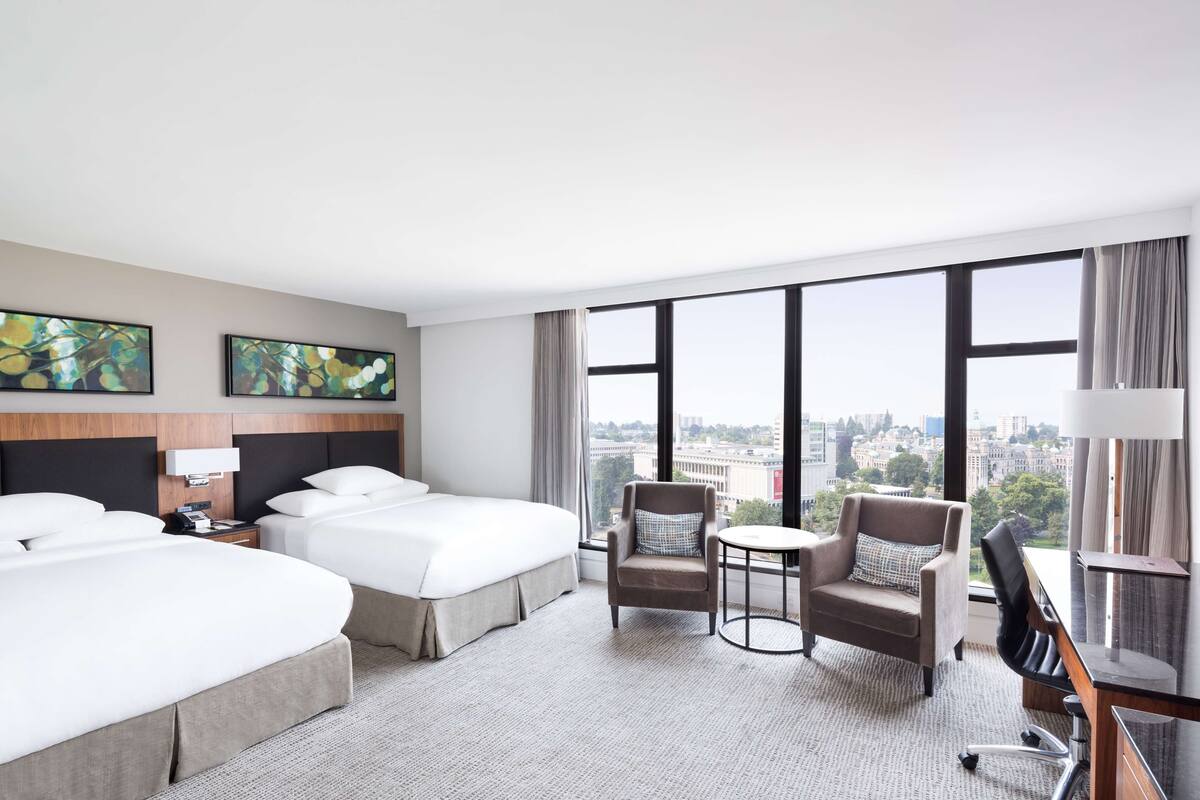 Habitación de hotel con dos camas, una mesita redonda pequeña, una silla y un escritorio con una lámpara.